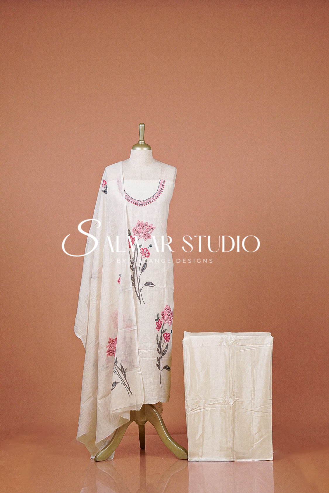 A cream-colored women's ethnic suit set  featuring a kurta with pink floral embroidery, a matching dupatta, and a folded bottom.
