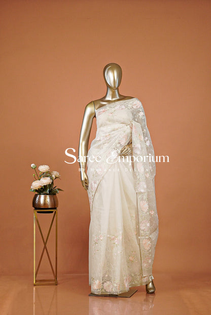 An off-white/cream embellished saree with a small gold stand holding flowers.