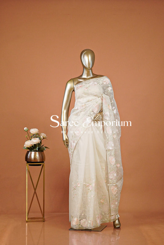 An off-white/cream embellished saree with a small gold stand holding flowers.