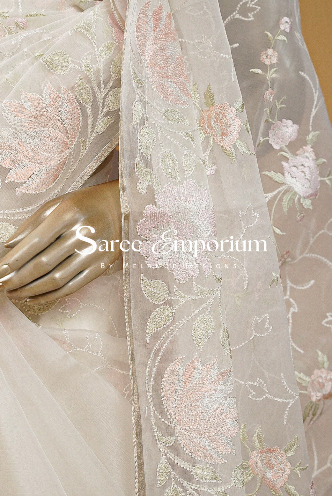A close-up of a sheer off-white organza saree or dupatta with delicate pink and green floral embroidery.