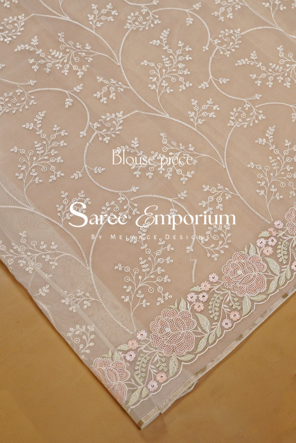 A close-up of a beige fabric with delicate white floral embroidery and a pink and green floral border.
