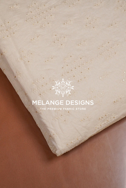 A folded cream-colored Premium Cora Cotton Fabric Dyeable with a subtle woven floral pattern.