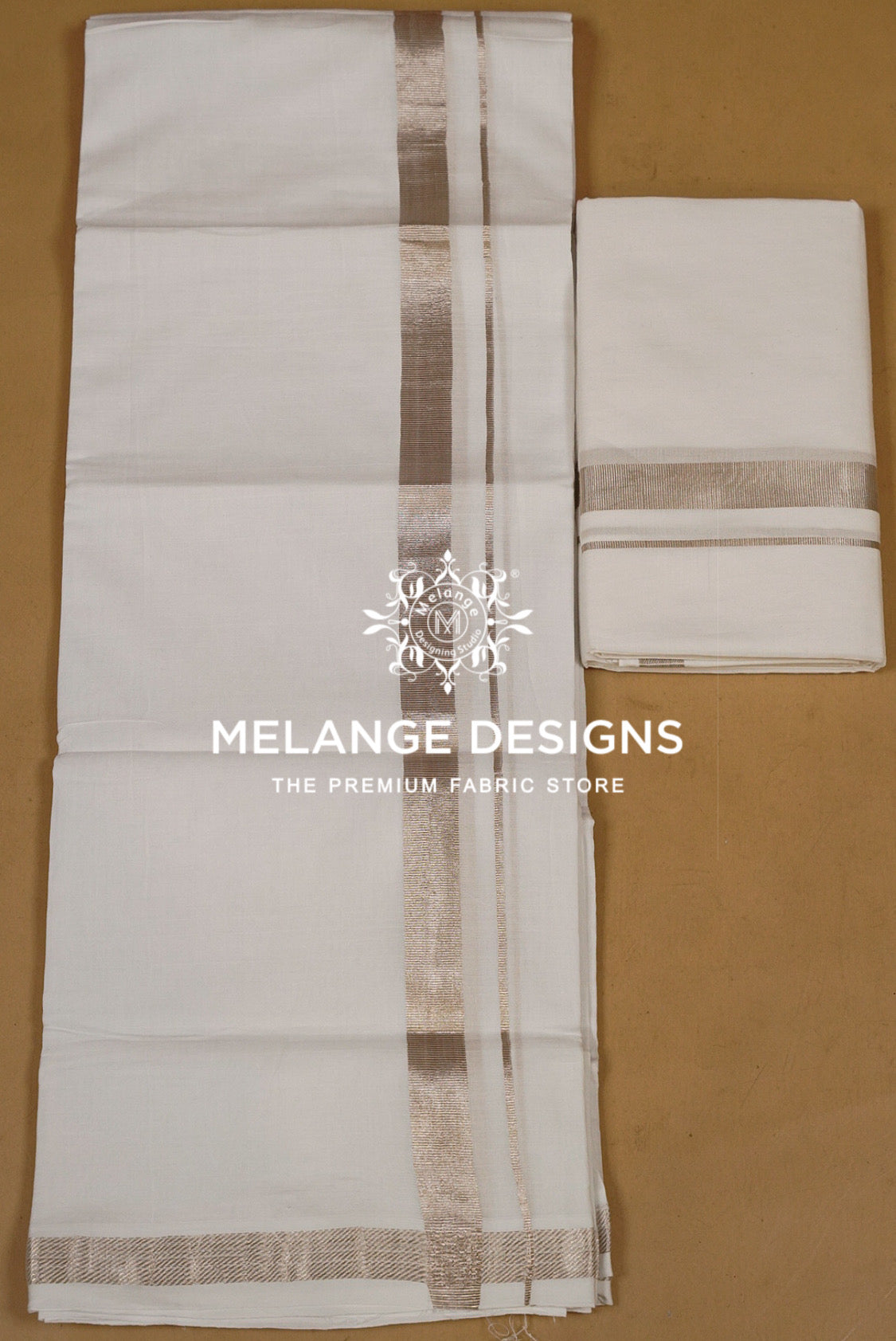 A white Indian cotton dhotis featuring a metallic gold border with a central vertical stripe and a matching folded piece of the dhotis on the right. 