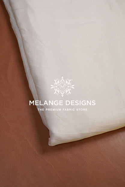 A close-up of a white Premium Viscose Organza Fabric Dyeable product, likely a pillowcase or folded textile, laid on a brown leather surface. 