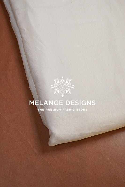 A close-up of a white Premium Viscose Organza Fabric Dyeable product, likely a pillowcase or folded textile, laid on a brown leather surface. 