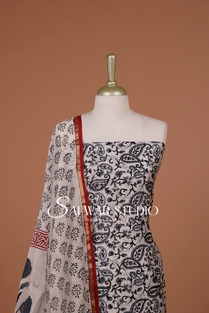 A sleeveless printed dress The garment has a black and white paisley and floral print with a red border detail along the neckline and drape.