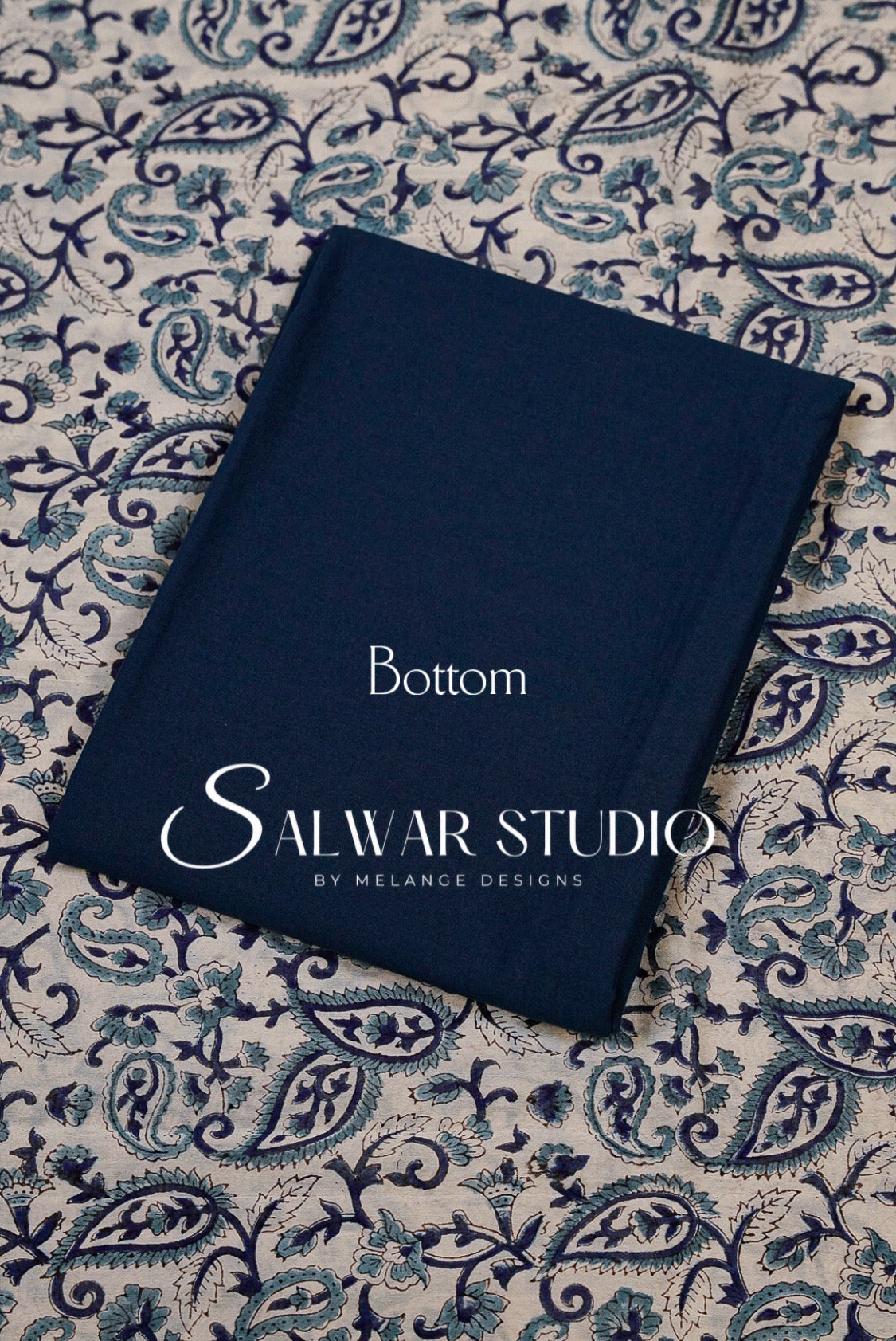 A navy blue fabric book or notebook titled 'Bottom'printed on the cover, placed diagonally on a blue and beige paisley patterned fabric .