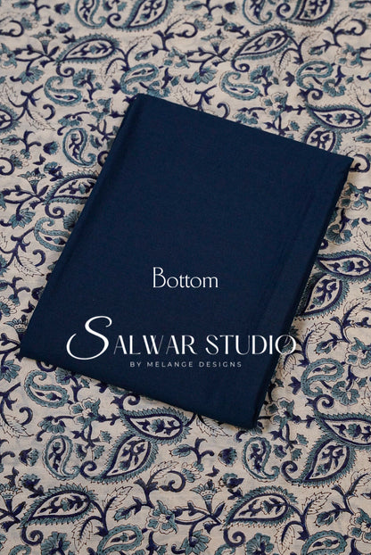 A navy blue fabric book or notebook titled 'Bottom'printed on the cover, placed diagonally on a blue and beige paisley patterned fabric .