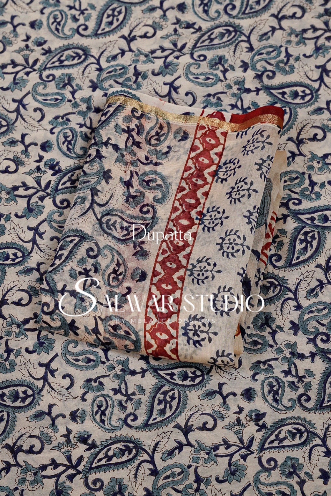A folded piece of printed fabric with a cream base, blue paisley and floral motifs, and a red vertical border.