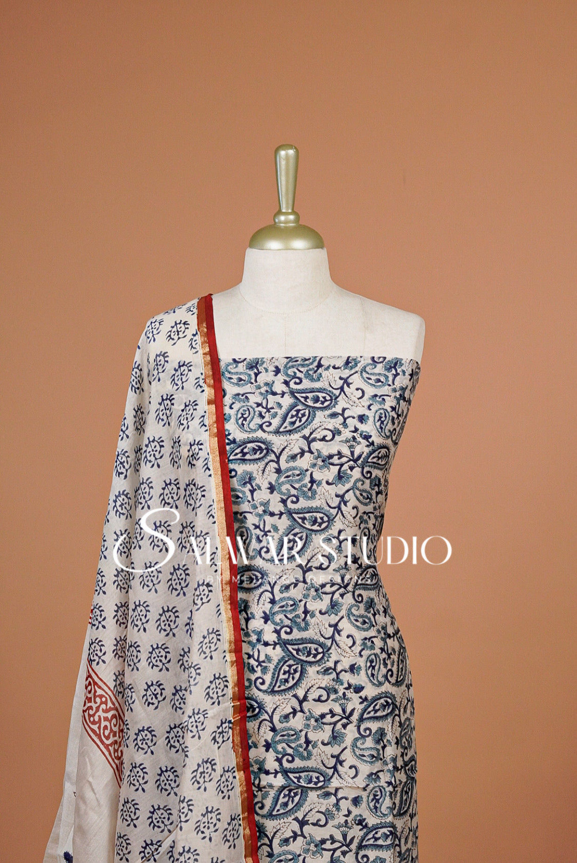 A sleeveless white and navy blue paisley printed dress displayed on a mannequin, paired with a matching patterned dupatta draped over the shoulder. The dupatta features a red border.