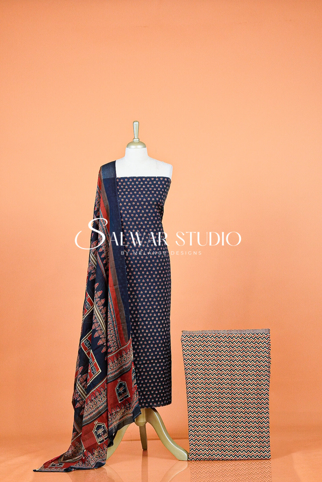 A three-piece women's salwar suit set The set includes a navy blue kurta with white polka dots, a matching navy dupatta with red and beige traditional patterns, and a beige and navy geometric patterned scarf.