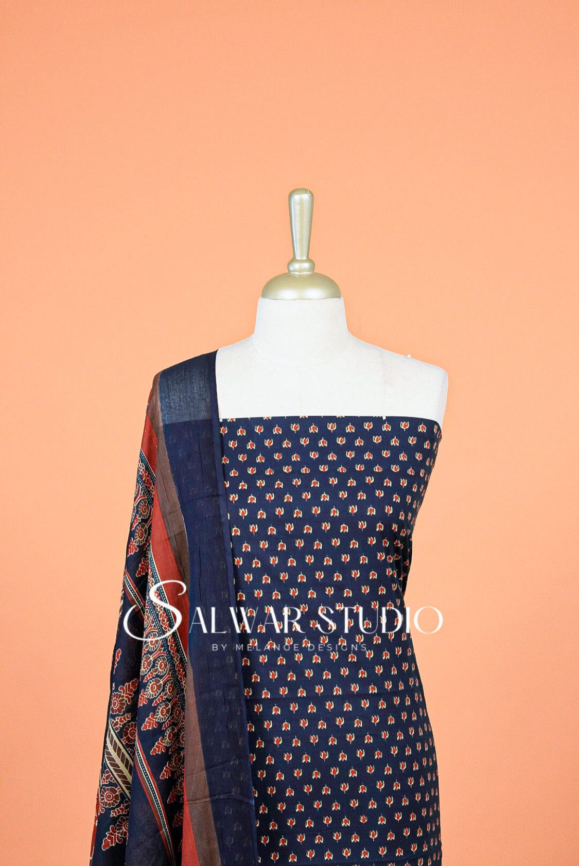A navy blue salwar suit fabric set with small orange and beige floral prints, displayed on a white dress form A matching patterned dupatta 