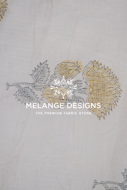 A close-up of a white Printed Cotton Cotta Fabric with a delicate embroidered floral pattern in gray and gold.
