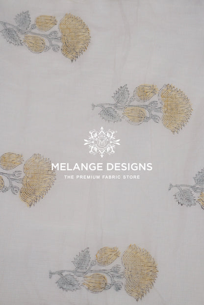 A close-up of a white Printed Cotton Cotta Fabric with a repeating block-printed floral pattern in muted gold and gray.