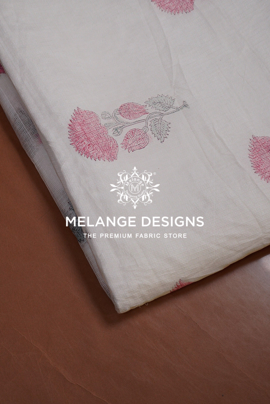 A folded piece of off-white Printed Cotton Cotta Fabric with pink and gray floral block prints, displayed diagonally on a brown wooden surface. 