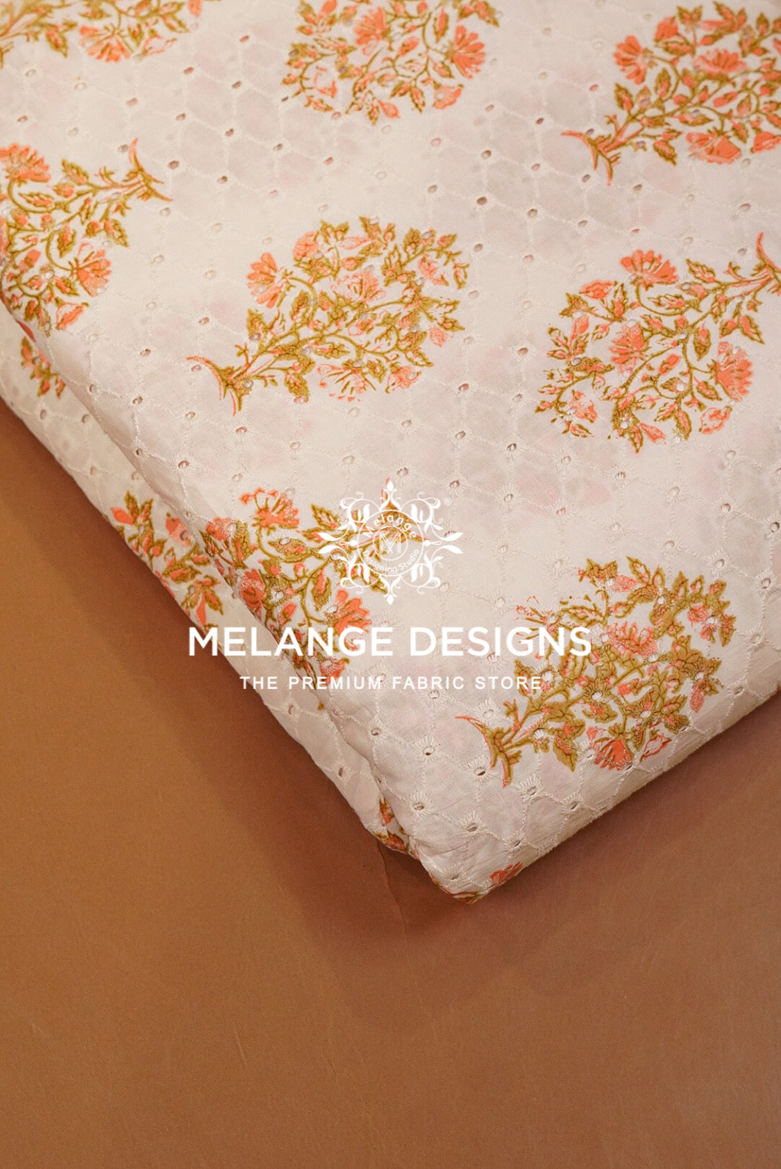 A close-up of folded Printed Cotton Hacoba Fabric with a cream base, eyelet embroidery, and a repeating floral pattern in peach and mustard yellow. 