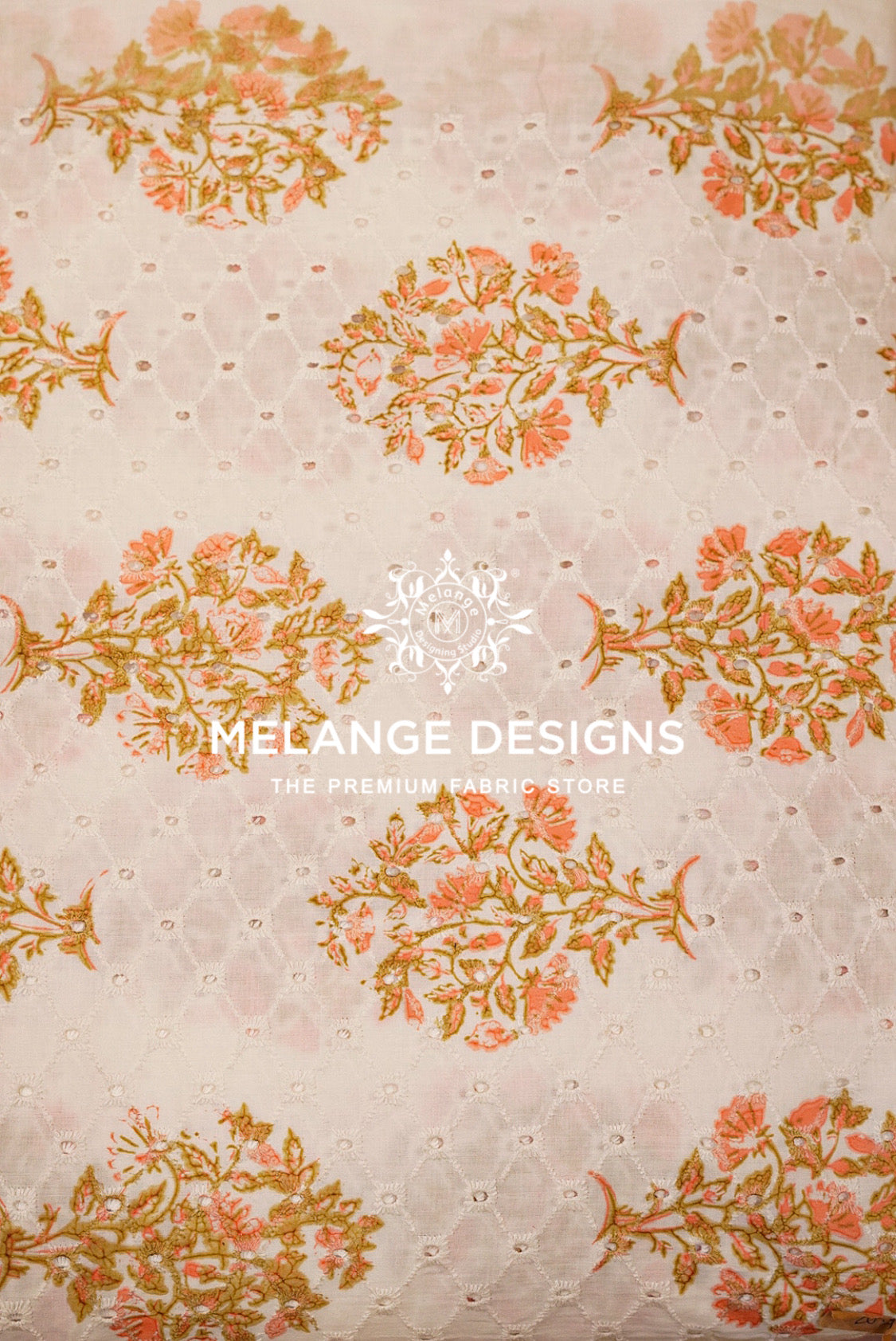 A close-up of a Printed Cotton Hacoba Fabric with a floral and geometric pattern. The fabric features a light beige base with a textured eyelet lace overlay and a repeating pattern of coral pink and mustard yellow floral motifs.