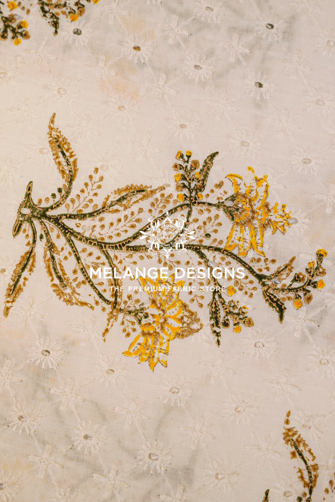 Close-up of a beige embroidered Printed Cotton Hacoba Fabricwith floral and leaf motifs in metallic gold and olive green.