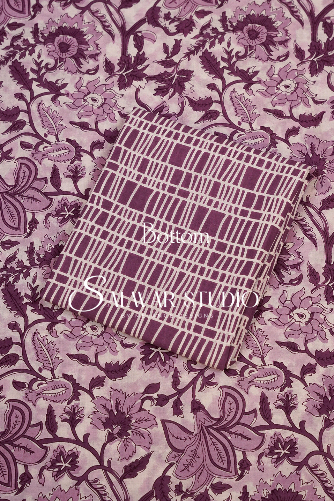 A folded piece of fabric with a purple and white grid pattern, placed on top of a matching floral printed fabric. 