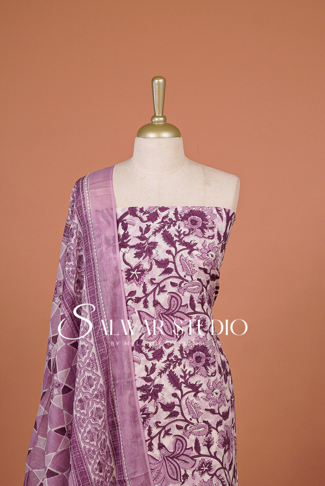 A lavender and purple floral printed salwar suit set.The set includes a printed salwar fabric, a solid lavender dupatta, and a matching printed border.
