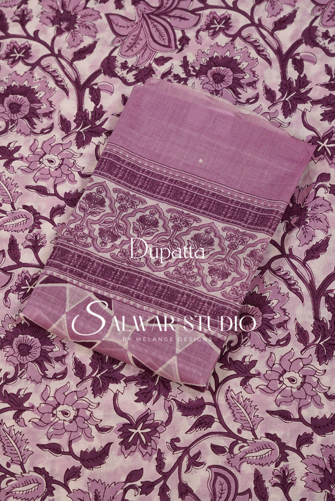 A folded dusty purple dupatta with intricate floral and paisley patterns, on top of a matching patterned fabric. 