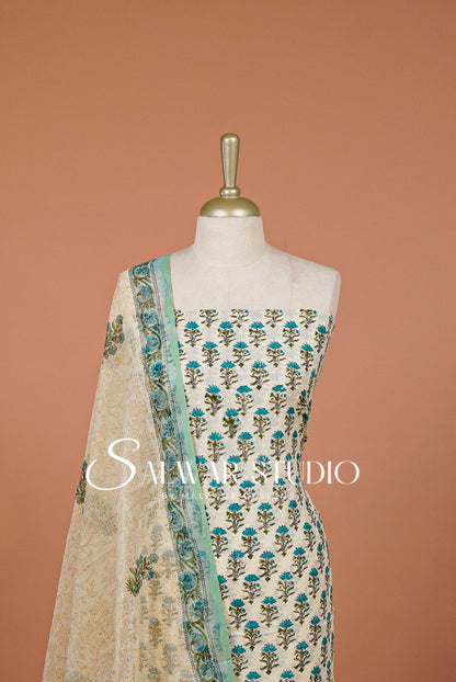 A cream-colored Indian ethnic salwar suit set .The set includes a printed kurta with teal and green floral motifs, a matching printed dupatta, and a light blue border on the kurta's edge.