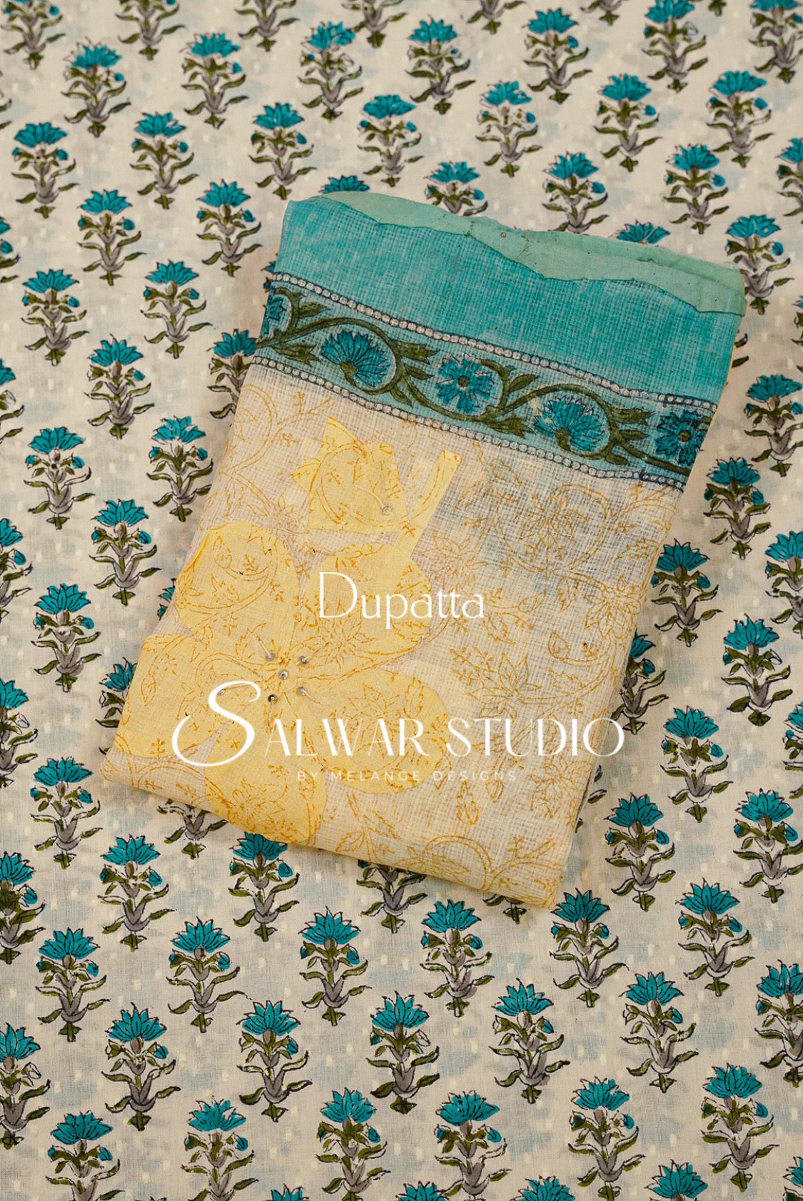 A folded dupatta fabric sample from Salwar Studio and a teal blue border with a dark green floral band.