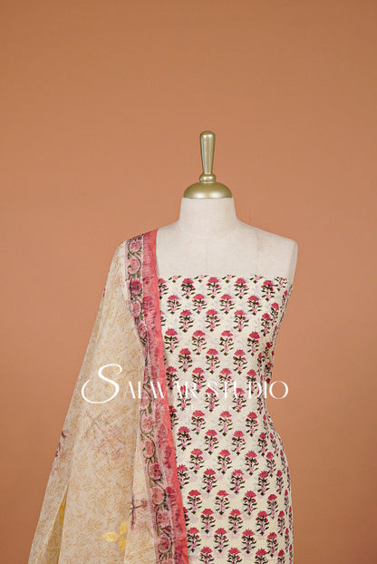 A cream-colored three-piece salwar kameez suit set .The set includes a printed kameez top with pink and green floral motifs, a beige dupatta with a pink border, and a matching beige printed bottom fabric.