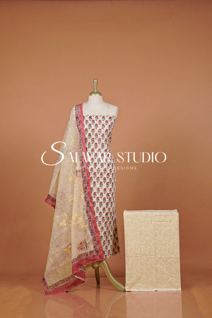 A traditional Indian salwar suit set . The set includes a beige printed salwar kameez with red and gold floral motifs, a matching beige dupatta with red borders, and a folded beige fabric piece.