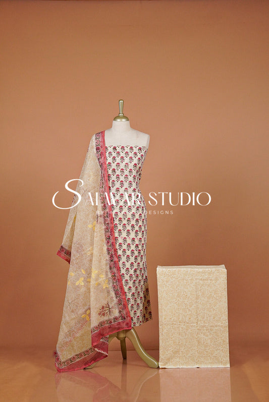 A traditional Indian salwar suit set . The set includes a beige printed salwar kameez with red and gold floral motifs, a matching beige dupatta with red borders, and a folded beige fabric piece.