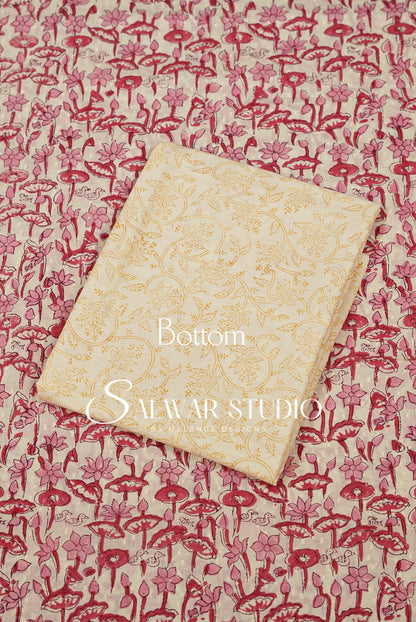 A folded cream-colored fabric piece with a gold floral pattern, placed diagonally on top of a matching printed fabric featuring red and pink floral motifs. 