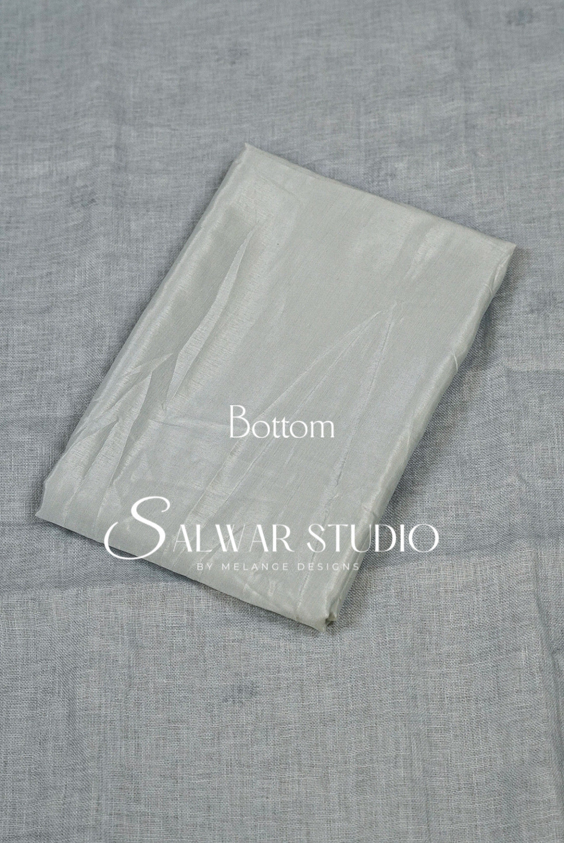 A folded light gray fabric piece, likely a dupatta or scarf, displayed on a textured gray fabric background. 