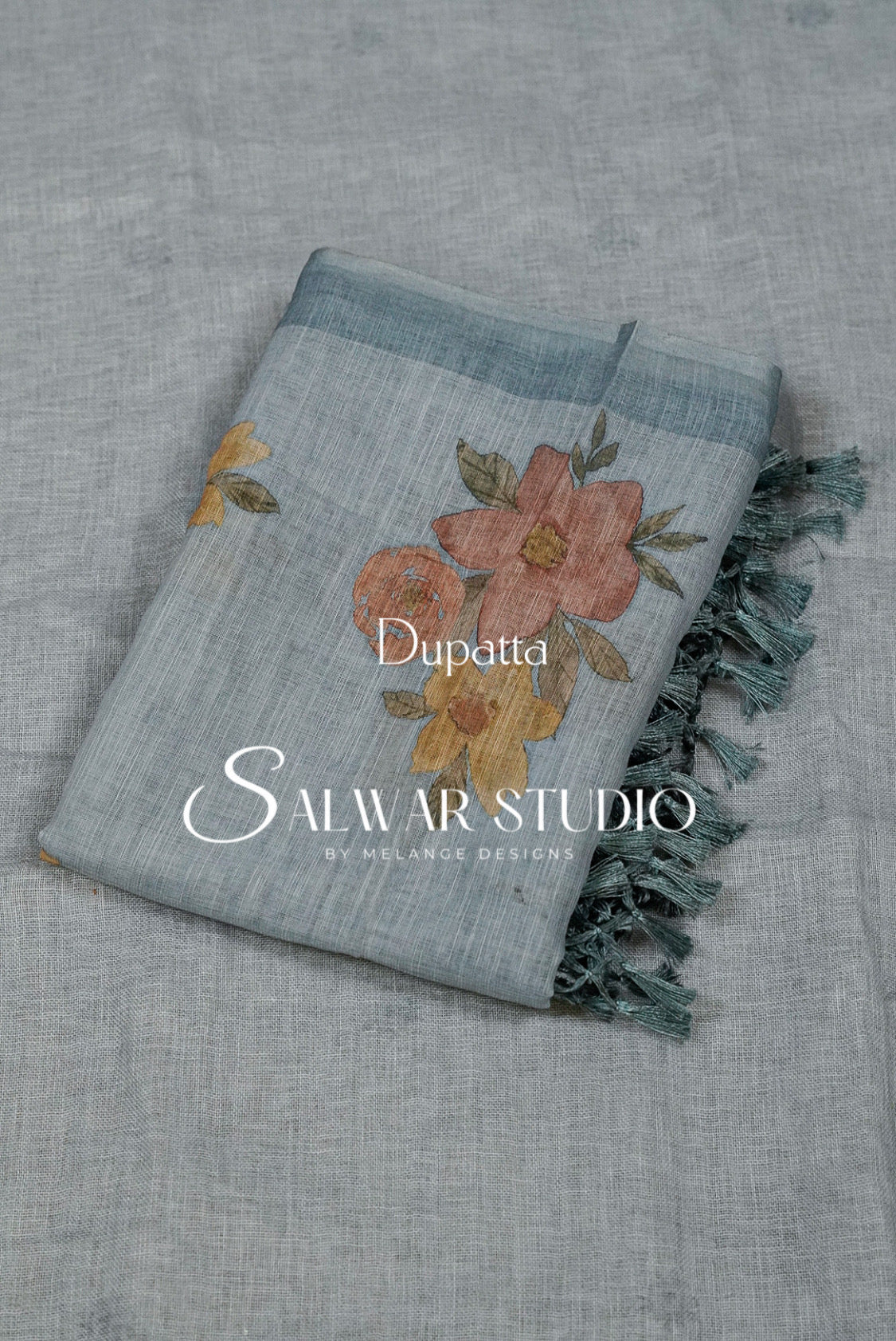 A folded light blue dupatta with a floral print in dusty pink, orange, and yellow, featuring dark teal fringe. 