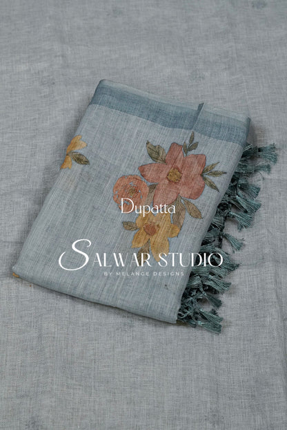 A folded light blue dupatta with a floral print in dusty pink, orange, and yellow, featuring dark teal fringe. 