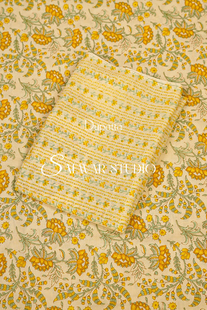 A folded piece of yellow and beige patterned fabric with green floral details, laid diagonally on top of a larger matching fabric sample. 