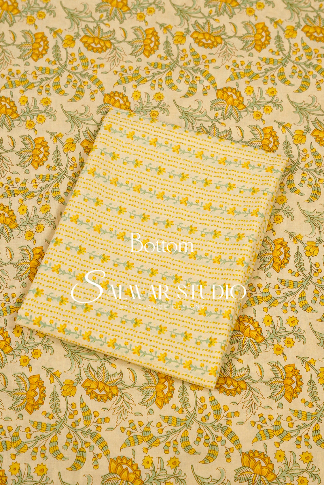 A folded cream-colored cotton fabric piece with a yellow and green floral pattern, displayed on top of a larger matching fabric sheet.