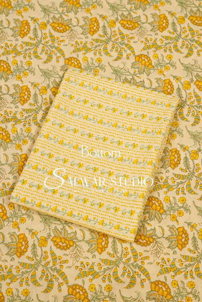 A folded cream-colored cotton fabric piece with a yellow and green floral pattern, displayed on top of a larger matching fabric sheet.