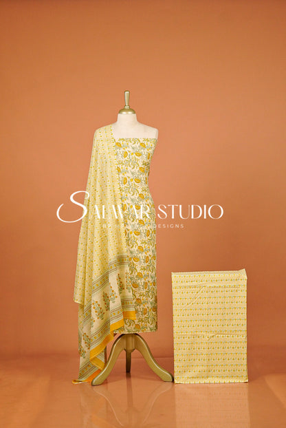 A yellow and white printed salwar suit set displayed on a mannequin, featuring a kurta, dupatta, and a folded fabric piece.