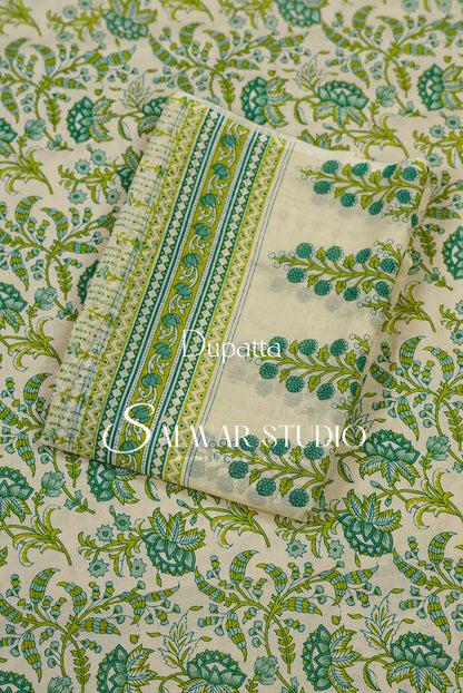 A folded piece of printed fabric with a green and teal floral block print on a cream base, laid diagonally over a matching larger sheet. The fabric features decorative borders with geometric patterns.