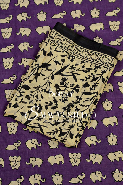 A folded beige fabric piece with a black floral and branch block print, laid diagonally on a purple background patterned with beige elephant silhouettes. 