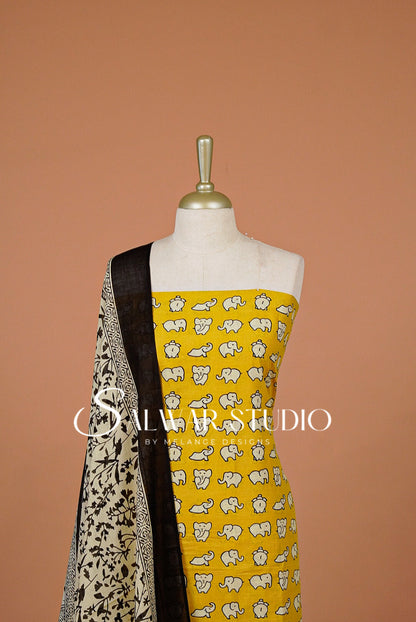 A yellow salwar suit fabric set . The set includes a yellow printed kurta with small elephant motifs, a black dupatta with white elephant prints, and a black border.