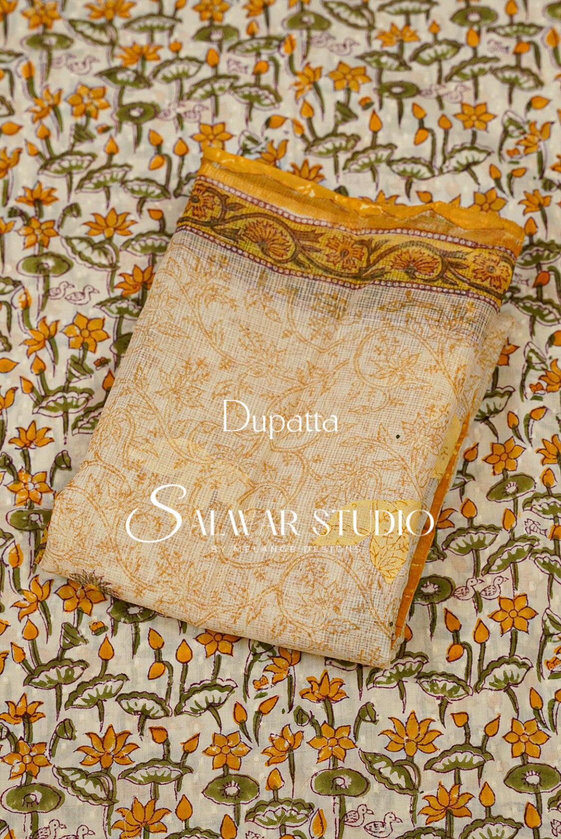 A folded dupatta fabric piece with a warm beige base and intricate yellow, orange, and green floral block print, displayed on top of a matching patterned fabric. 