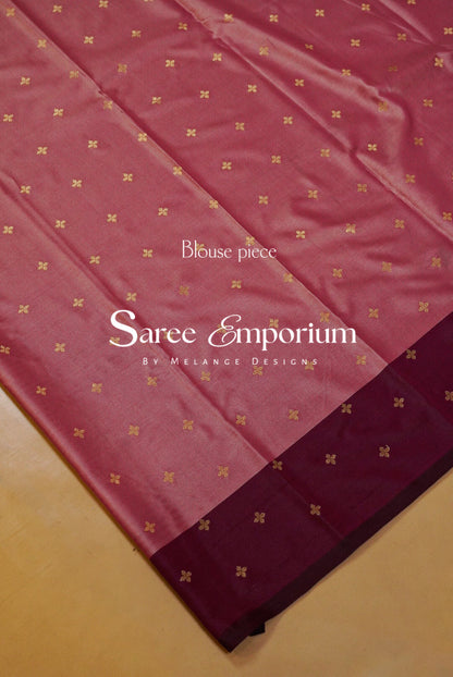 A close-up of a pinkish-red saree fabric with a border in a darker maroon shade, decorated with small gold motifs.