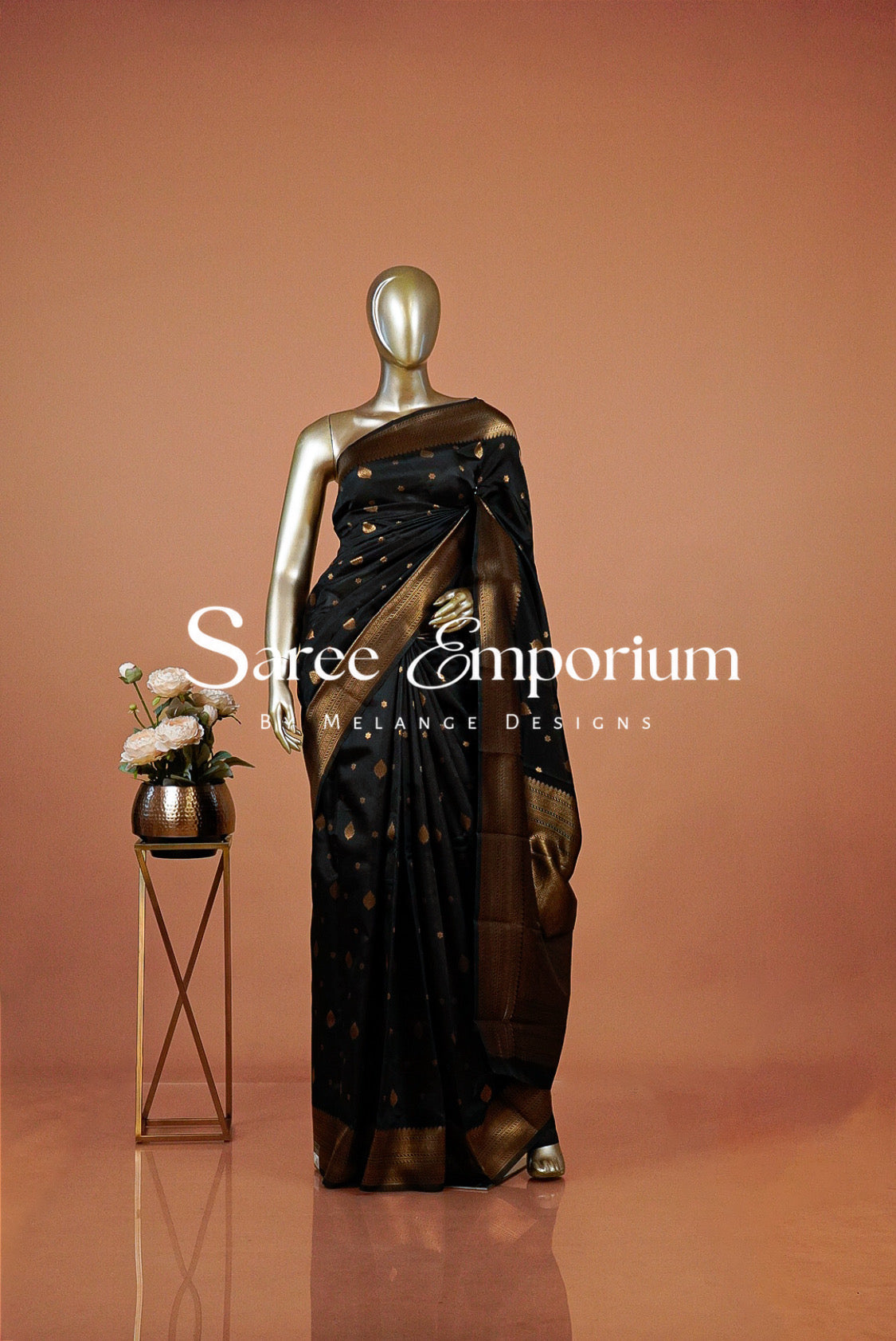 A metallic mannequin displays a black saree with gold motifs and a brown border .
