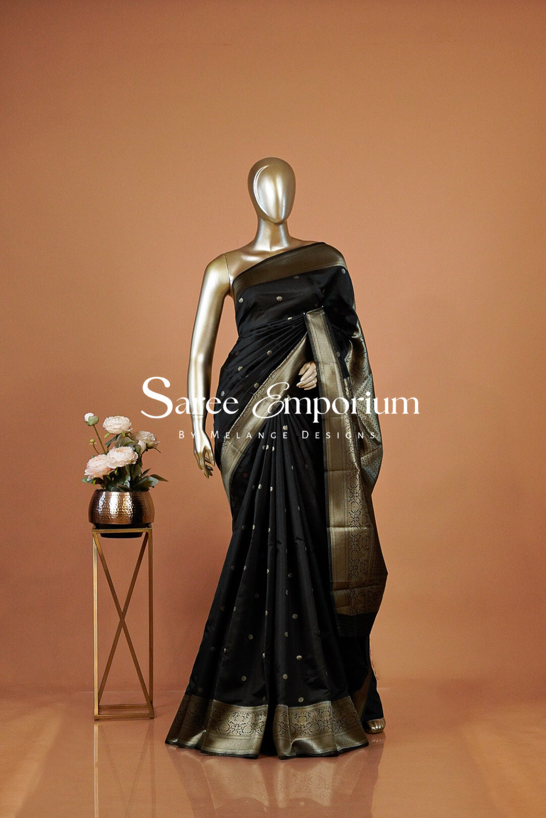 A black saree with gold zari detailing and a gold border .