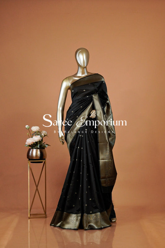 A black saree with gold zari detailing and a gold border .