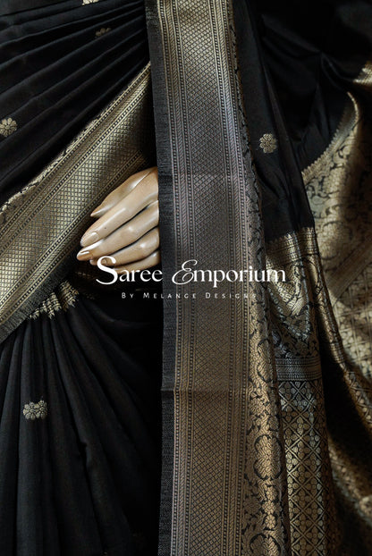 A close-up of a black silk saree with intricate gold zari brocade work .