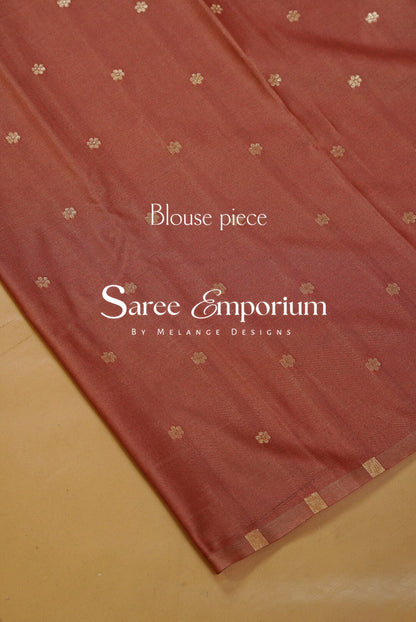 A close-up of a terracotta-colored saree blouse piece with small gold floral motifs and a gold border.