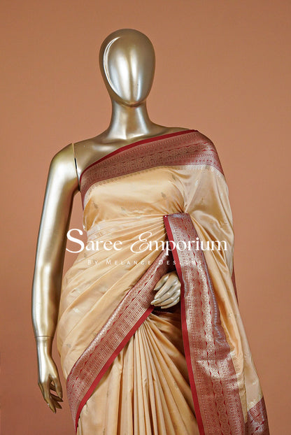 A beige silk saree with a metallic red border and pallu.