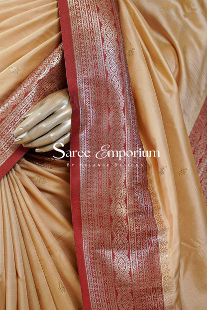 A close-up of a beige silk saree with a prominent red and gold zari border.